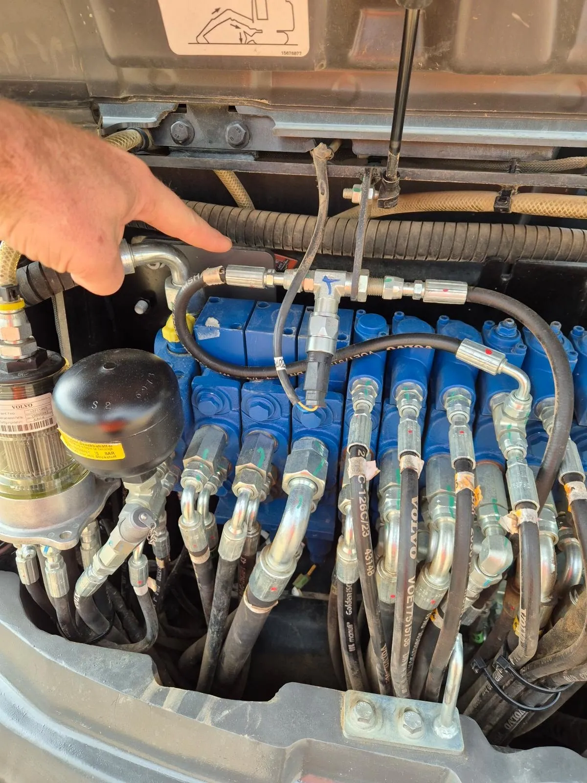 Mechanic pointing to a fitting on an excavator hydraulic valve bank during a hydraulic repair in Queanbeyan