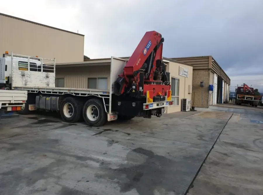 Isuzu flatbed truck fitted with a red Palfinger vehicle loading crane outside the Queanbeyan workshop
