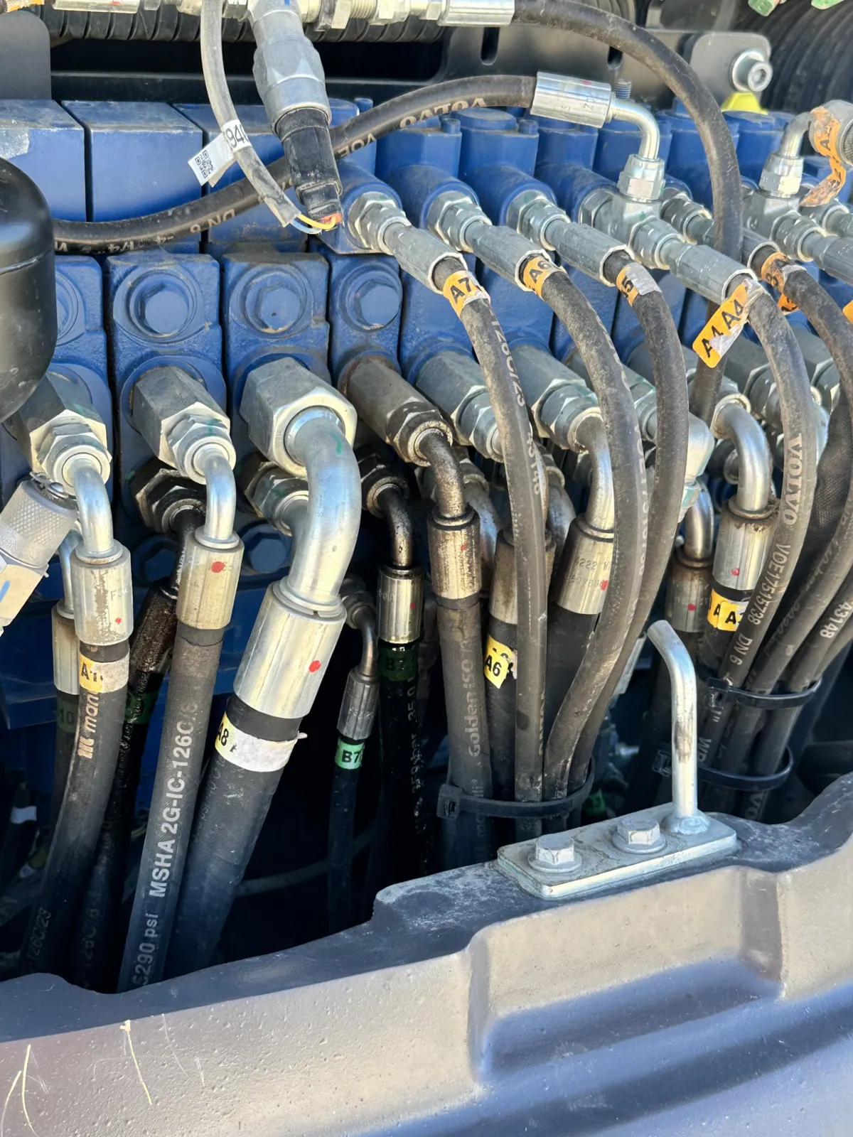 Hydraulic valve bank with colour-tagged hoses and fittings during a hydraulic repair in Canberra