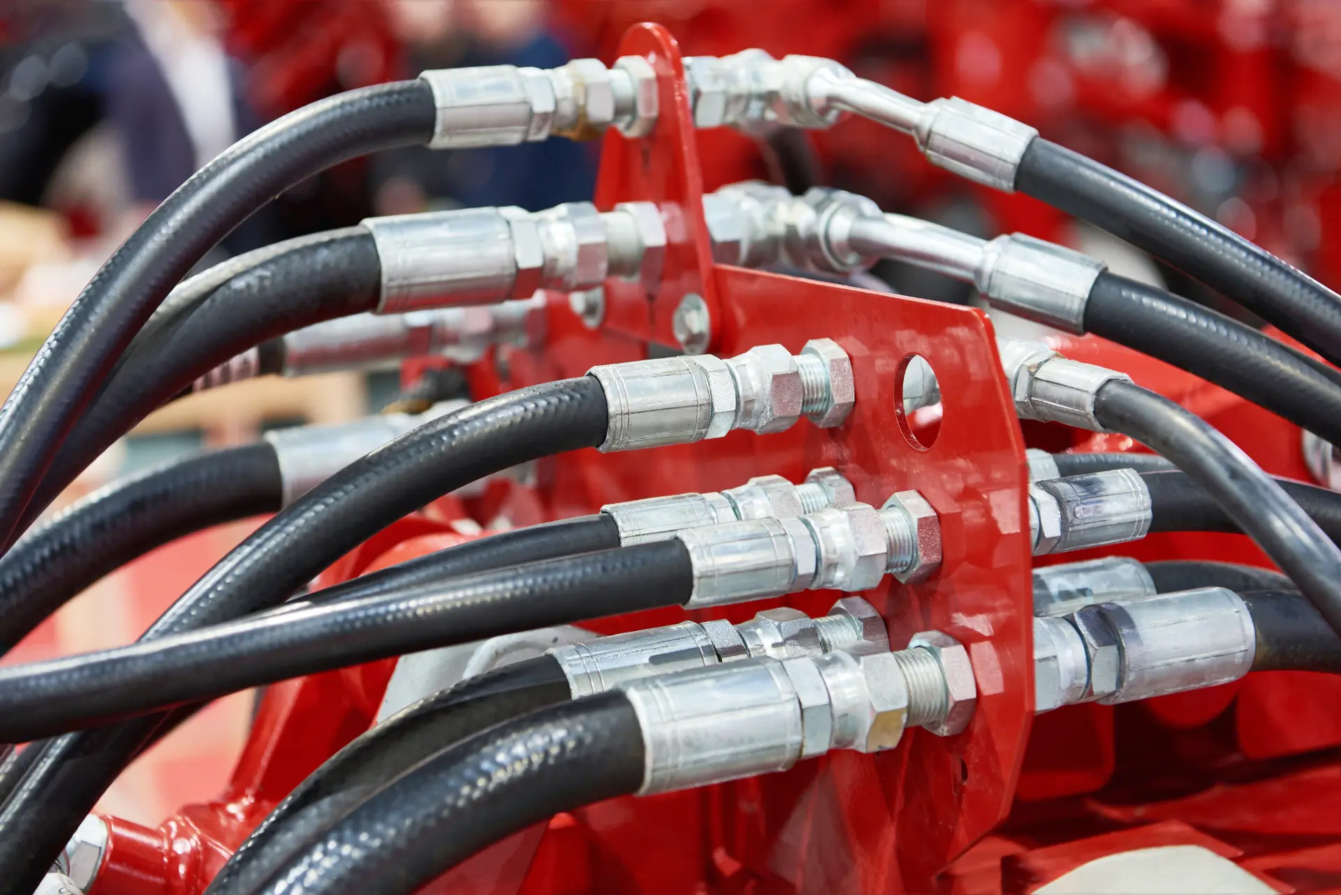 Hydraulic hoses with crimped steel fittings connected to a red machine manifold